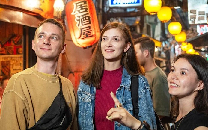 Shinjuku bar hopping tour group exploring vibrant alley with lanterns in Tokyo.