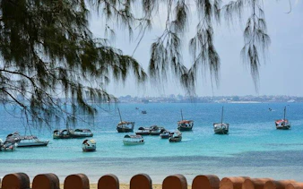 Boats anchored in the turquoise waters of Stone Town, Zanzibar, with distant shoreline.