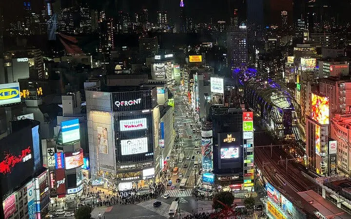 Shibuya Crossing at night, Tokyo, with illuminated buildings and bustling streets.