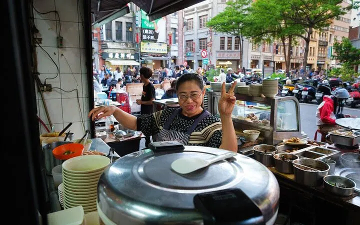 Local vendor at a Taipei street food stall during a food tour, with dishes and bustling street in view.
