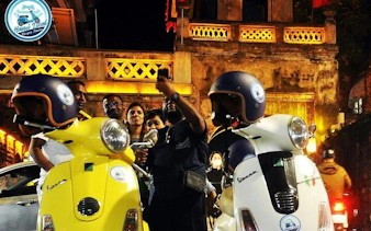 Group enjoying Hanoi street food tour on Vespas at night, vibrant city backdrop.