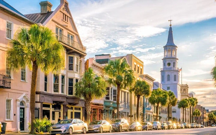Historic Charleston street with colorful buildings and palm trees, featuring a prominent church steeple.