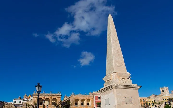 Obelisk in Menorca town square under clear blue sky.