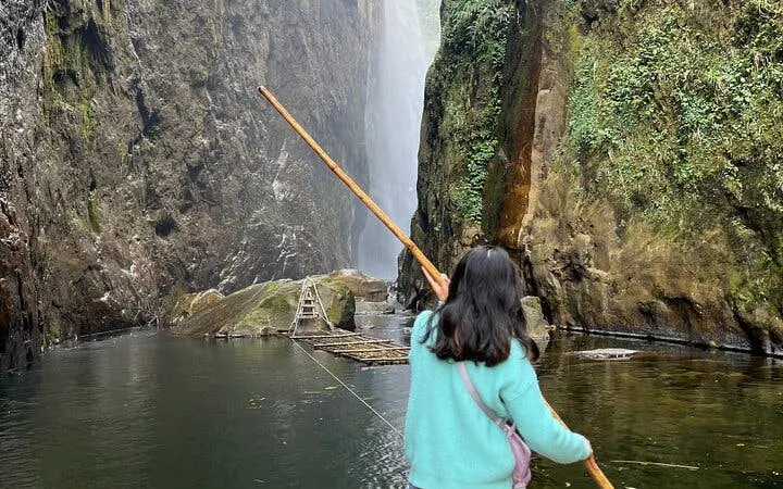 Person holding a stick near Dragon Waterfall in Sapa, surrounded by cliffs and water.