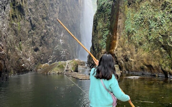Person holding a stick near Dragon Waterfall in Sapa, surrounded by cliffs and water.