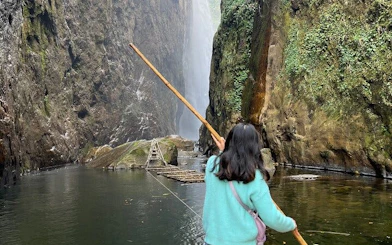 Person holding a stick near Dragon Waterfall in Sapa, surrounded by cliffs and water.
