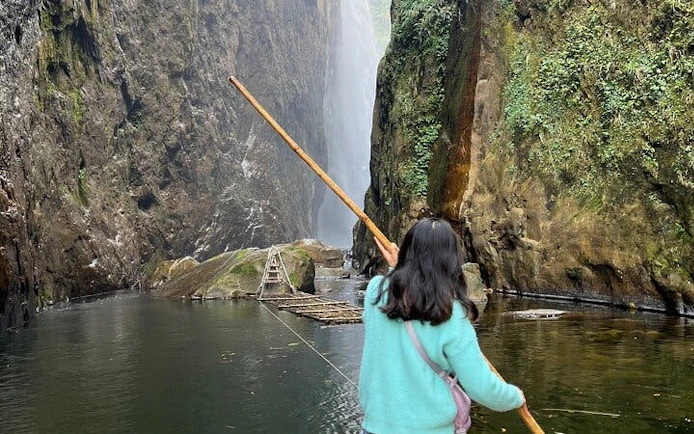 Person holding a stick near Dragon Waterfall in Sapa, surrounded by cliffs and water.