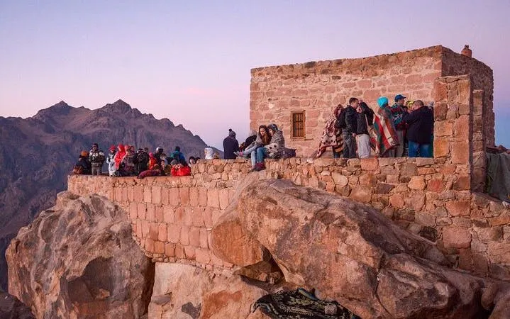 Visitors gather at a stone building on Moses Mountain during sunrise, part of the Saint Catherine Monastery tour.