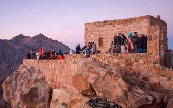 Visitors gather at a stone building on Moses Mountain during sunrise, part of the Saint Catherine Monastery tour.