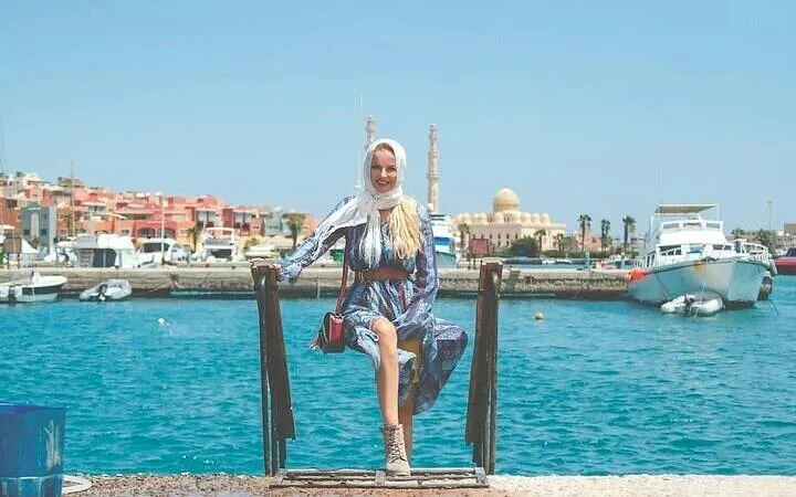 Woman sitting by the marina with boats and mosque in Hurghada, Egypt.