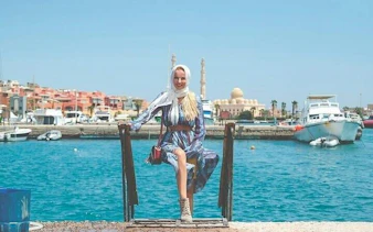 Woman sitting by the marina with boats and mosque in Hurghada, Egypt.