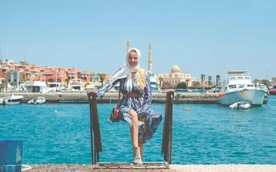 Woman sitting by the marina with boats and mosque in Hurghada, Egypt.