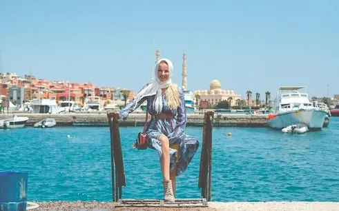 Woman sitting by the marina with boats and mosque in Hurghada, Egypt.