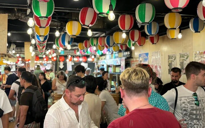 Crowd exploring Nishiki Market in Kyoto with colorful lanterns overhead.