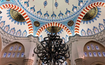Ornate mosque ceiling with intricate patterns and chandelier in Tirana, featured on self-guided walking tour app.