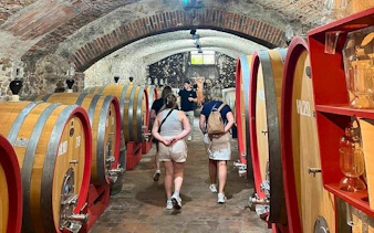 Tourists exploring a Tuscan winery cellar with large wooden barrels.
