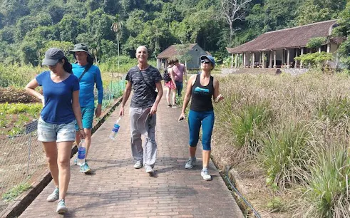Group trekking on a path through lush greenery near traditional buildings in Cat Ba, Vietnam.