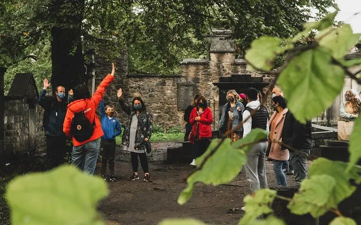 Group on Harry Potter walking tour in Edinburgh cemetery, guide leading interactive trivia game.
