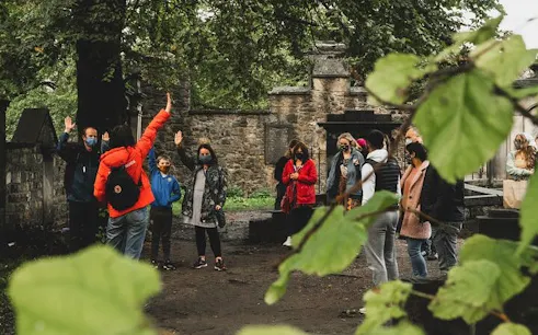 Group on Harry Potter walking tour in Edinburgh cemetery, guide leading interactive trivia game.
