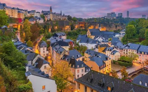 Luxembourg cityscape at dusk with historic buildings and lush greenery, part of a self-guided audio tour.