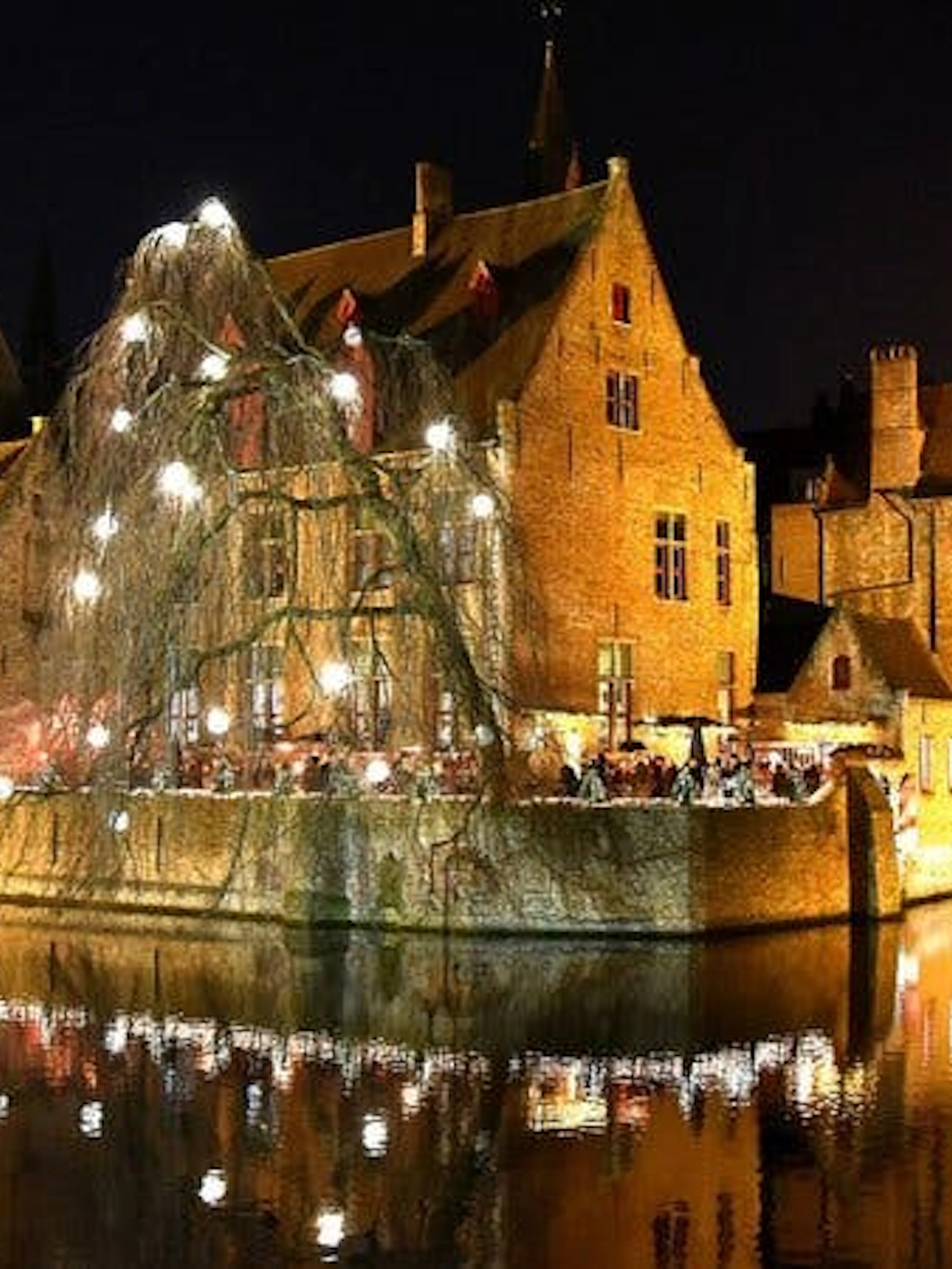 Bruges canal-side buildings illuminated at night, part of self-guided walking tour via mobile app.