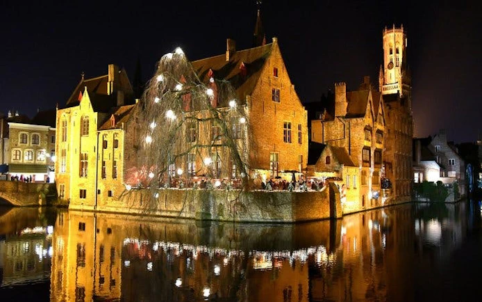 Bruges canal-side buildings illuminated at night, part of self-guided walking tour via mobile app.