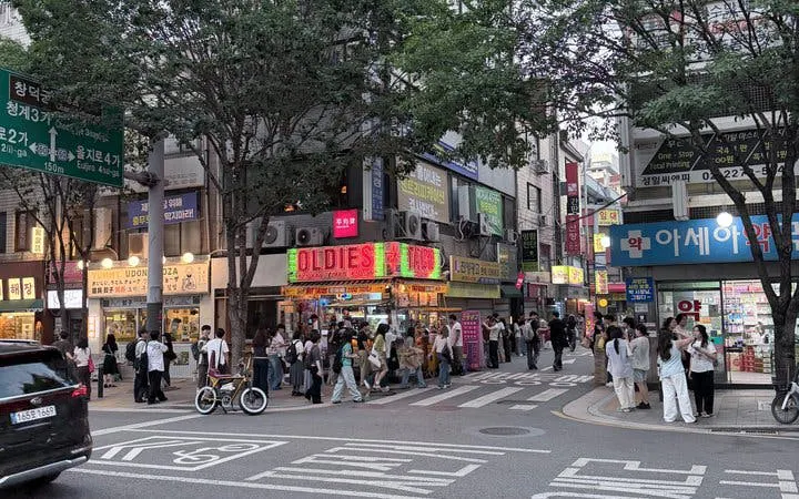 Seoul street scene with people outside restaurants and shops, highlighting Chimaek night food experience.