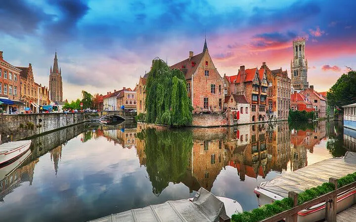 Bruges canal with historic buildings and Belfry tower at sunset, part of self-guided city exploration game.