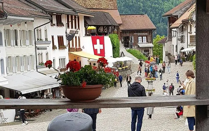 Gruyères village square with Swiss flag, tourists exploring cobblestone streets, Zurich tour.