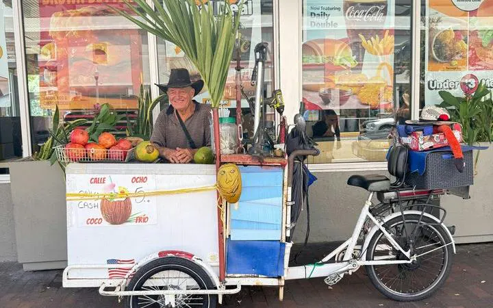 Street vendor with fruit cart on Calle Ocho, Little Havana, Miami, offering coconuts and tropical produce.