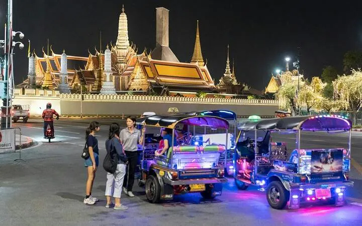 Tuk tuks parked near illuminated temple in Bangkok during night street food tour.