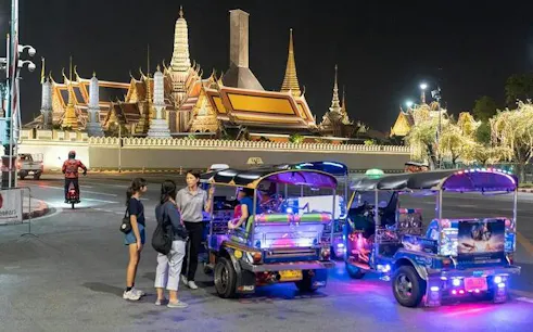 Tuk tuks parked near illuminated temple in Bangkok during night street food tour.
