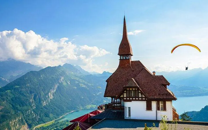 Paraglider over Lake Brienz with Swiss chalet and Bernese Alps in background, Lucerne tour.