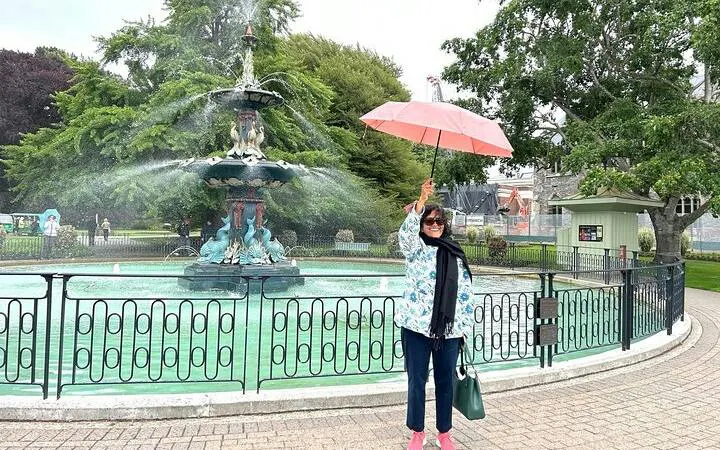Person holding umbrella by Peacock Fountain in Christchurch Botanic Gardens during city tour.