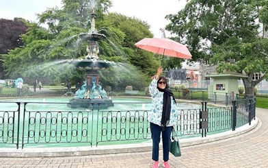 Person holding umbrella by Peacock Fountain in Christchurch Botanic Gardens during city tour.