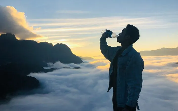 Silhouette of a person drinking water at sunrise over clouds in Sa Pa, Vietnam.