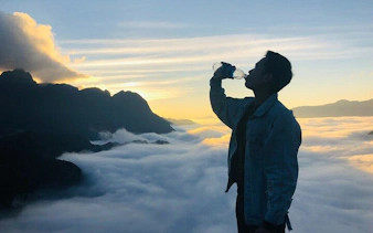 Silhouette of a person drinking water at sunrise over clouds in Sa Pa, Vietnam.