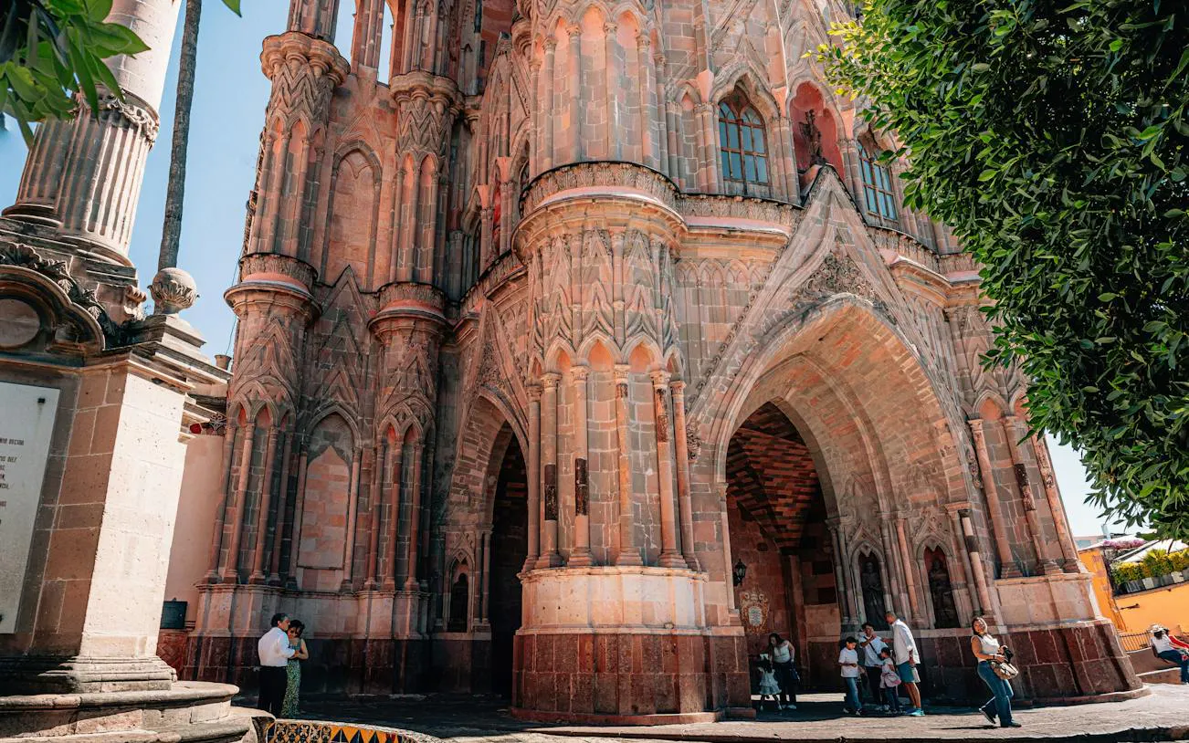 Parroquia de San Miguel Arcángel facade in San Miguel de Allende, Mexico, with visitors nearby.