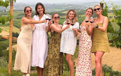 Group enjoying wine tasting in Tuscany vineyard with scenic view of San Gimignano.