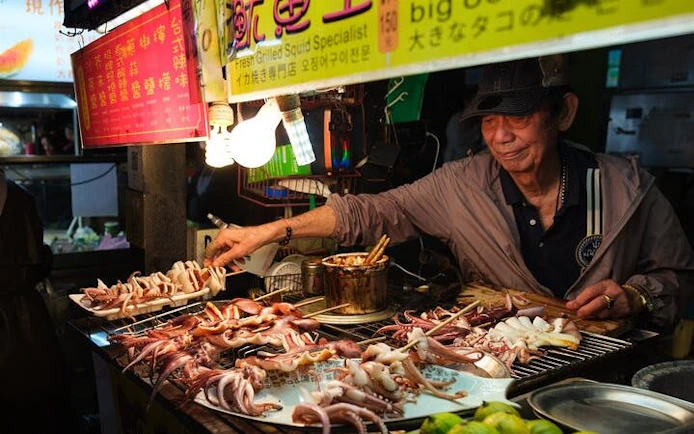 Vendor grilling squid at a Taipei night market food tour.
