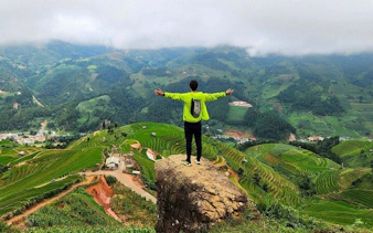 Person standing on a rock overlooking terraced rice fields in Sapa, Vietnam.