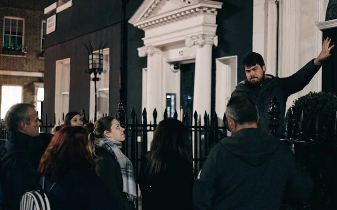 Tour guide narrating haunted history to a group outside a historic York building at night.