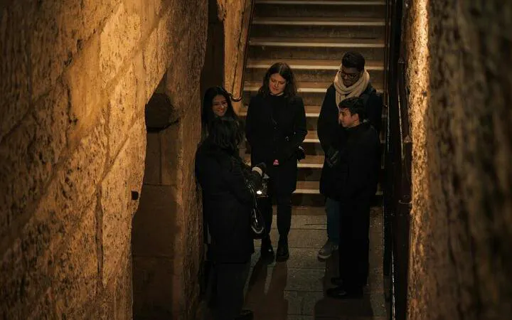 Tour group in dimly lit Paris alley during evening ghost walking tour.