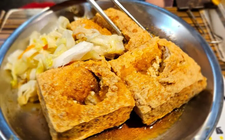 Stinky tofu with pickled cabbage served on a metal plate in Taipei food tour.