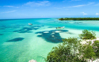 Boats on turquoise waters near Punta Mosquito, Holbox Island, with lush greenery and clear skies.