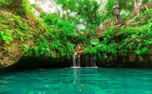 Visitors sitting by a waterfall in a lush cenote on a snorkeling tour in America.