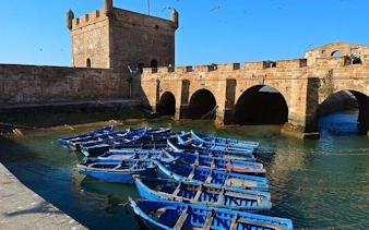 Essaouira harbor with blue boats and historic fortress, part of Marrakesh day trip.