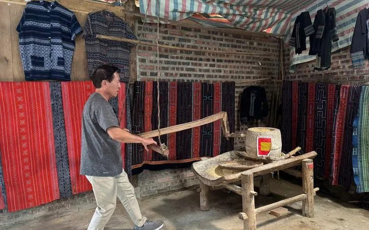 Man using traditional mill in Sapa village, surrounded by colorful textiles.