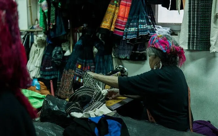 Local artisan sewing traditional garments in Sapa workshop during food tour experience.