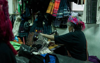 Local artisan sewing traditional garments in Sapa workshop during food tour experience.